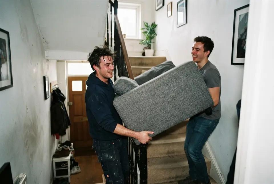 Two movers carrying a sofa up a flight of stairs